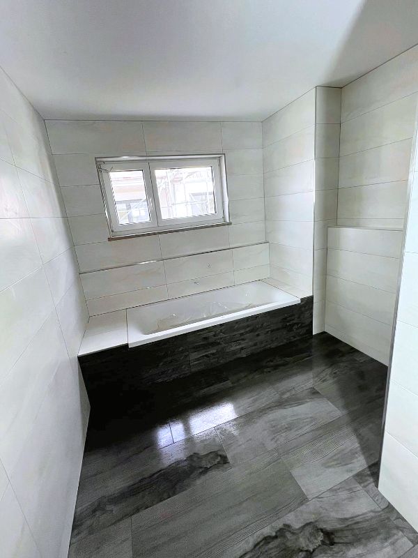 Badezimmer mit Badewanne und hellen Fliesen sowie grauem Boden nach Renovierung in Ingolstadt von Renovierung & Sanierung ALBAN