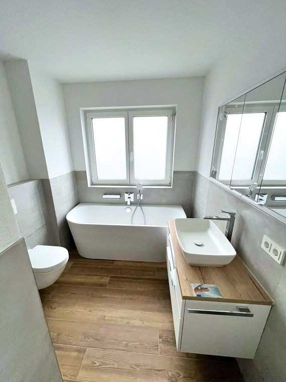 Badezimmer mit Badewanne, Waschbecken und Holzboden nach Renovierung in Ingolstadt von Renovierung & Sanierung ALBAN