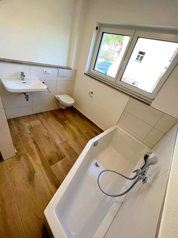 Badezimmer mit Badewanne, Waschbecken, WC und Holzboden nach Renovierung in Ingolstadt von Renovierung & Sanierung ALBAN
