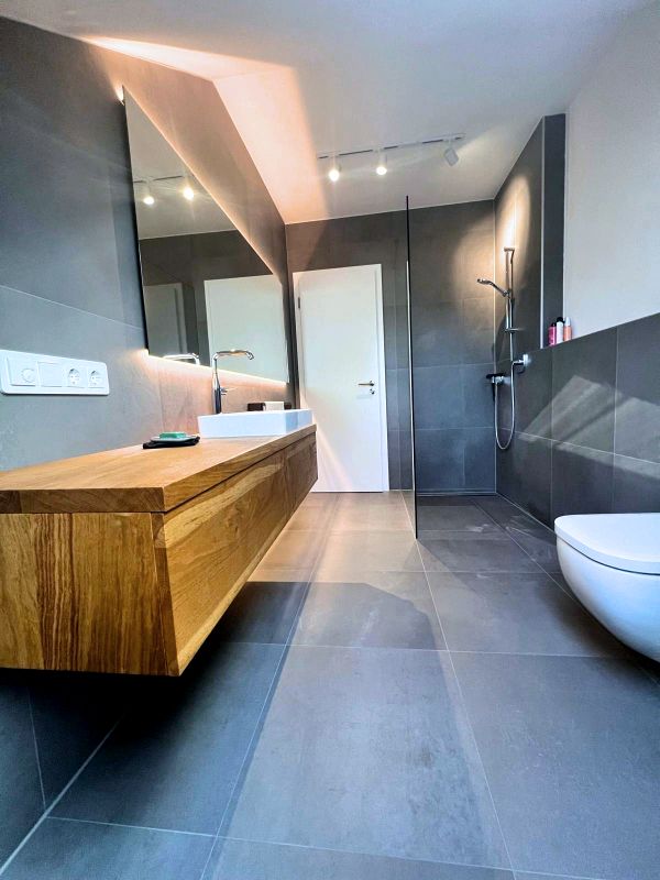 Modernes Badezimmer mit Dusche, Waschbecken und Holzmöbeln nach Renovierung in Ingolstadt von Renovierung & Sanierung ALBAN