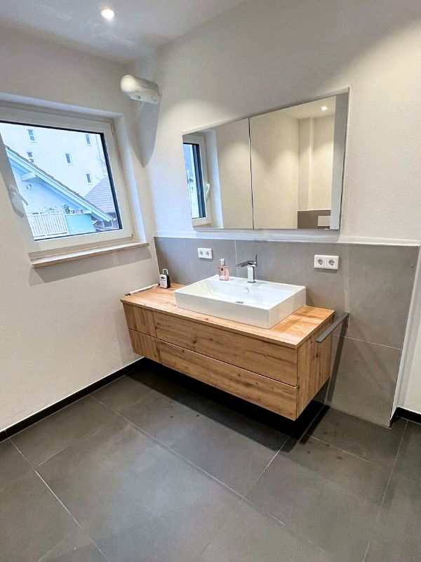 Badezimmer mit Waschbecken, Holzmöbeln und Spiegelschrank nach Renovierung in Ingolstadt von Renovierung & Sanierung ALBAN