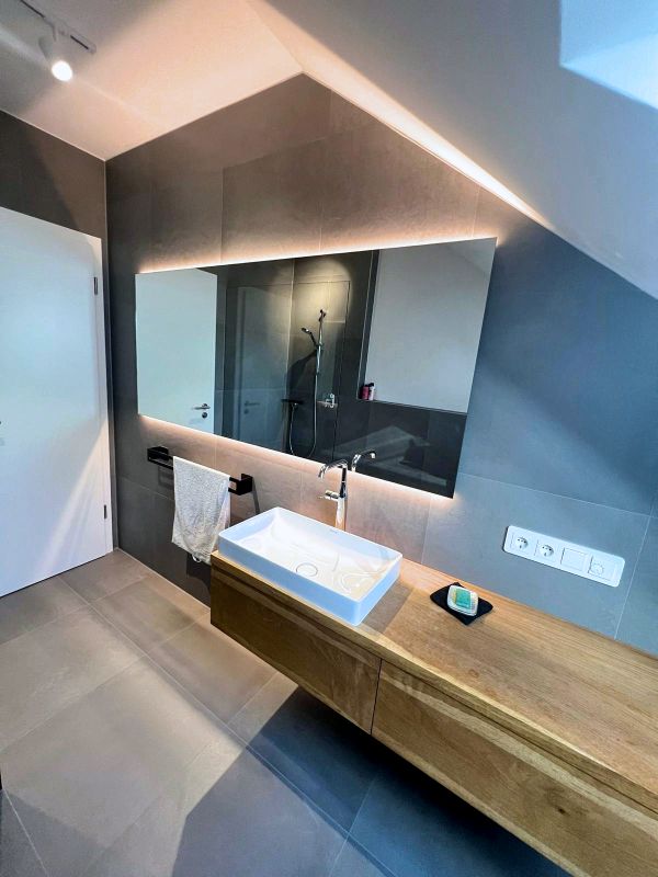 Badezimmer mit Waschbecken, großem Spiegel und Holzmöbeln nach Renovierung in Ingolstadt von Renovierung & Sanierung ALBAN