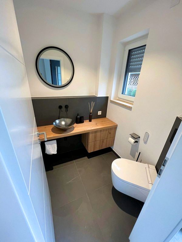 Modernes Gäste-WC mit Waschbecken, Holzmöbeln und Spiegel nach Renovierung in Ingolstadt von Renovierung & Sanierung ALBAN